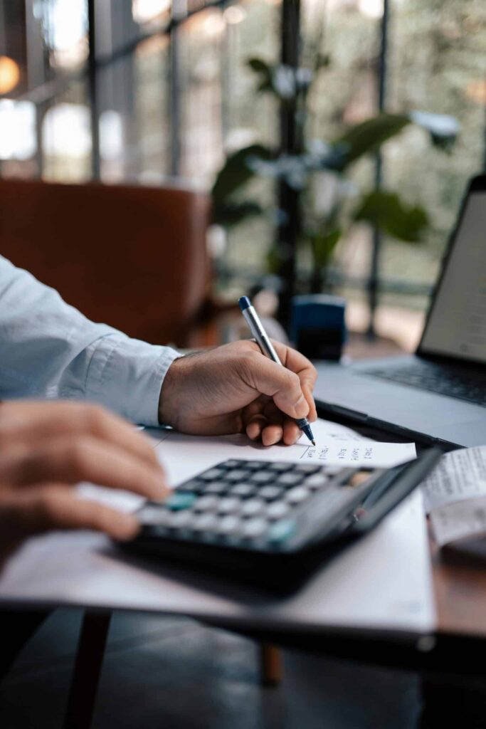 Free A person calculating finances with a calculator and pen on a desk indoors. Stock Photo